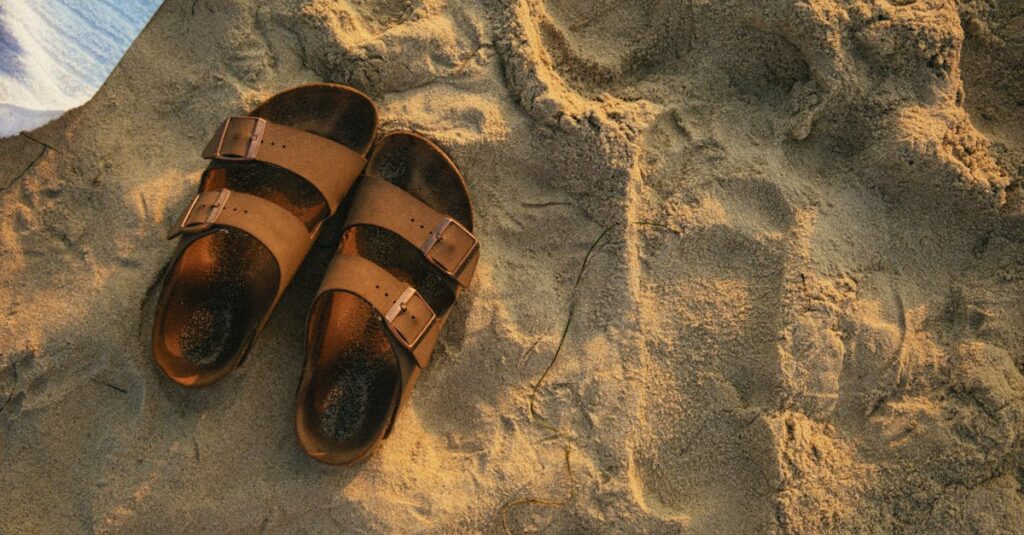 Top view of leather sandals on a sandy beach during sunrise, exuding a warm vacation vibe.